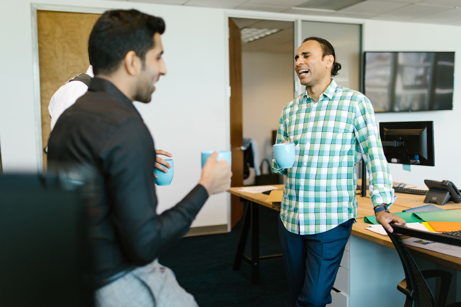 Coworkers laughing over coffee in a bright room