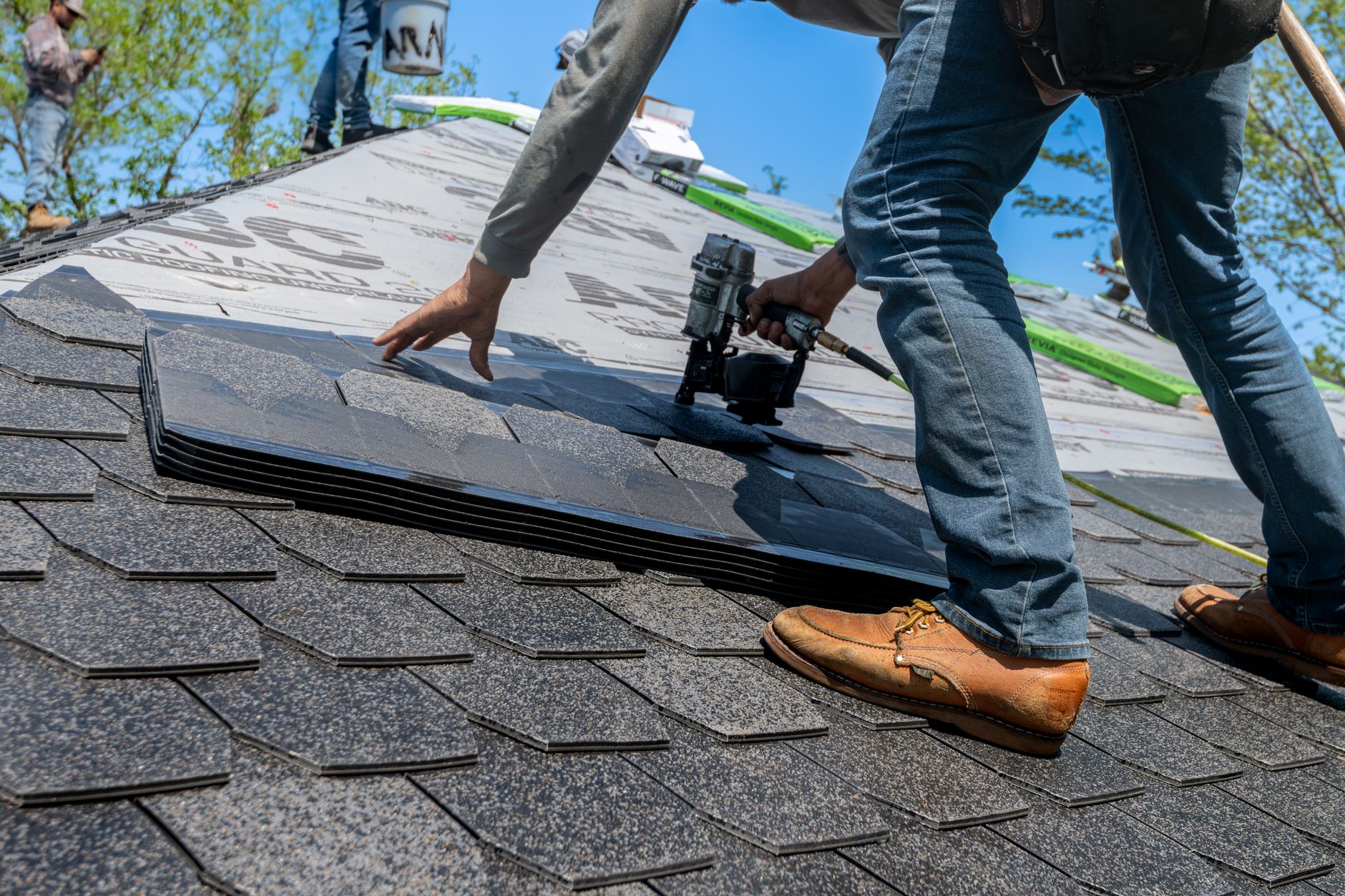 A roofer using a nail gun to set shingles on a residential roof