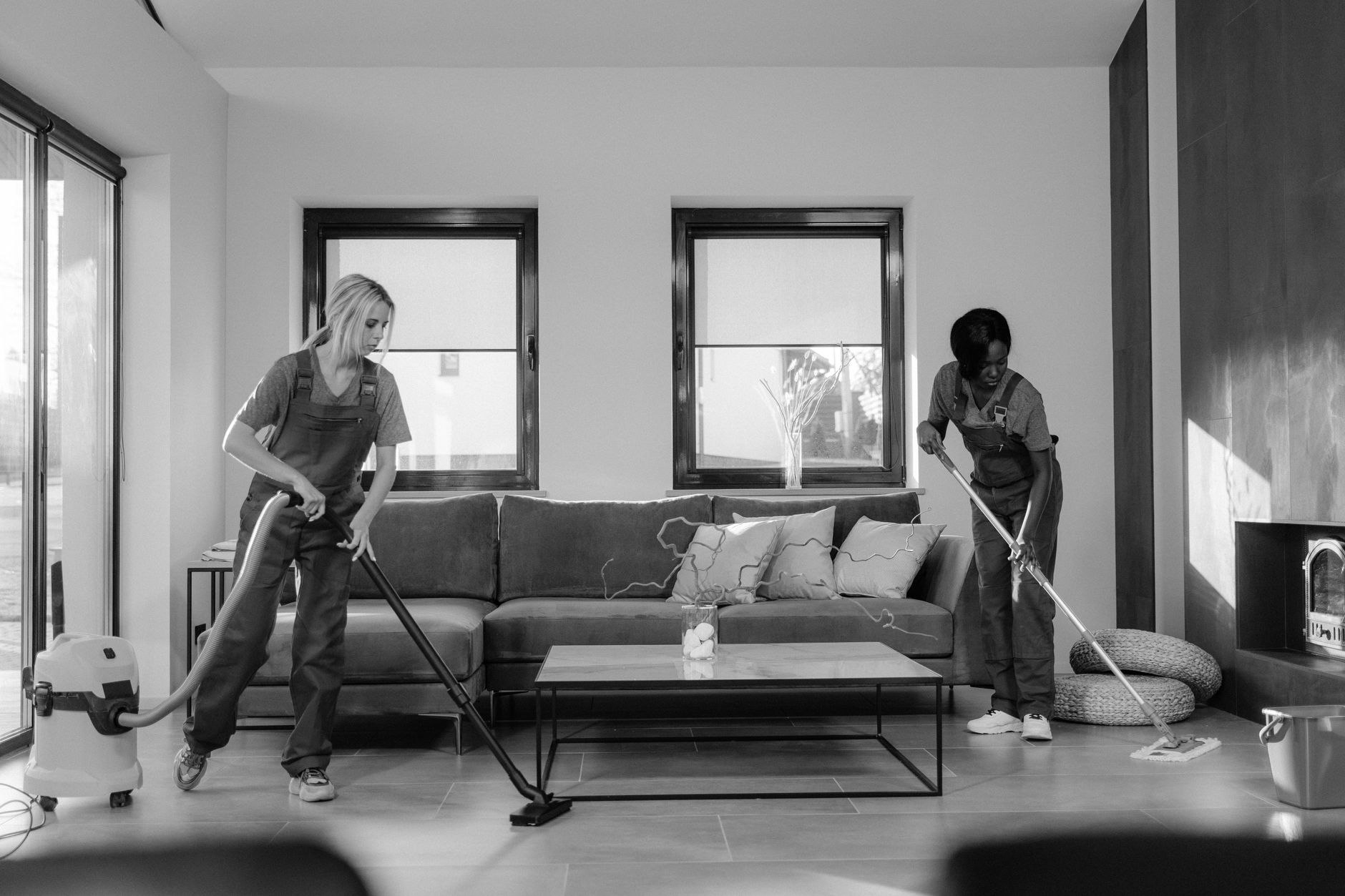 Two cleaners working in a living room with a vacuum and a mop