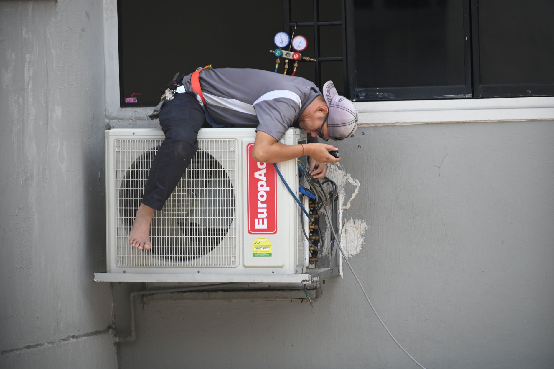 A technician repairing an outdoor air conditioning unit mounted on a building wall